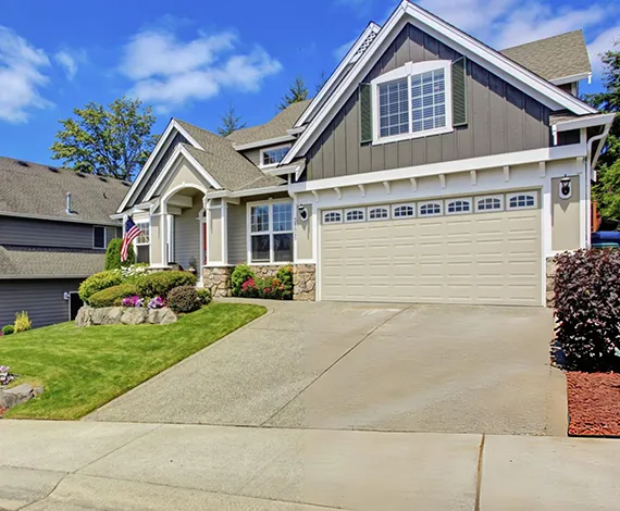 A modern suburban house with a white garage door, green lawn, and a driveway leading to the entrance.