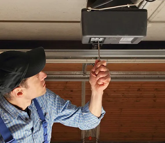 Technician adjusting a garage door opener mechanism inside a garage.