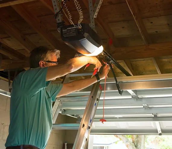 A technician in a green shirt working on a garage door mechanism inside a garage.