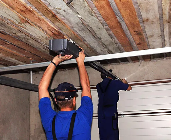 A garage technician in a blue uniform working on a garage door mechanism.