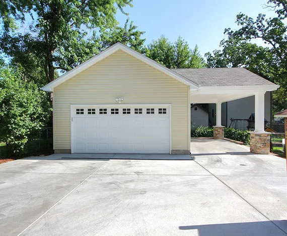 White garage door installed on a modern suburban home with a driveway and green trees.