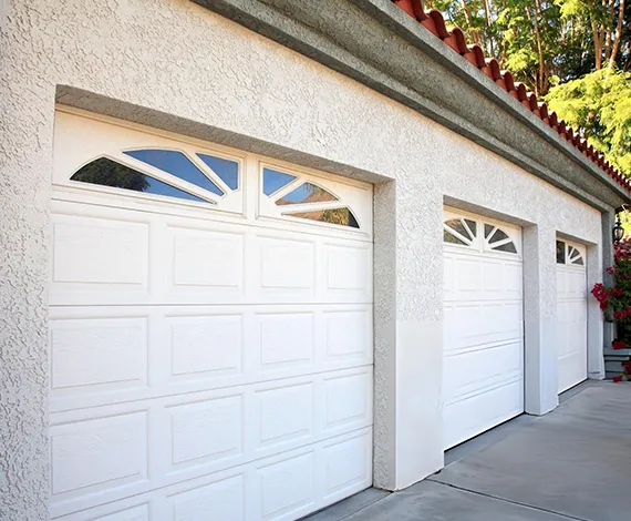 A white double garage door with decorative windows installed on a suburban home with a driveway.