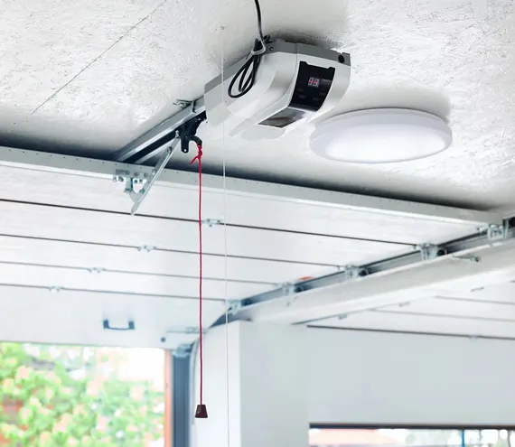 Interior view of a garage ceiling featuring a mounted garage door opener with a red emergency release cord.