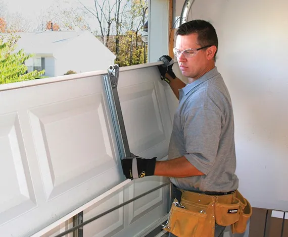 Technician repairing a garage door, adjusting its mechanism with tools.