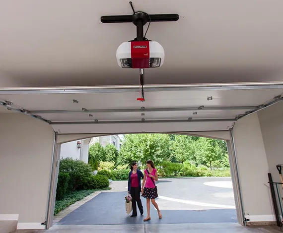 An open garage with a ceiling fan, leading to a driveway where two people are visible outside.